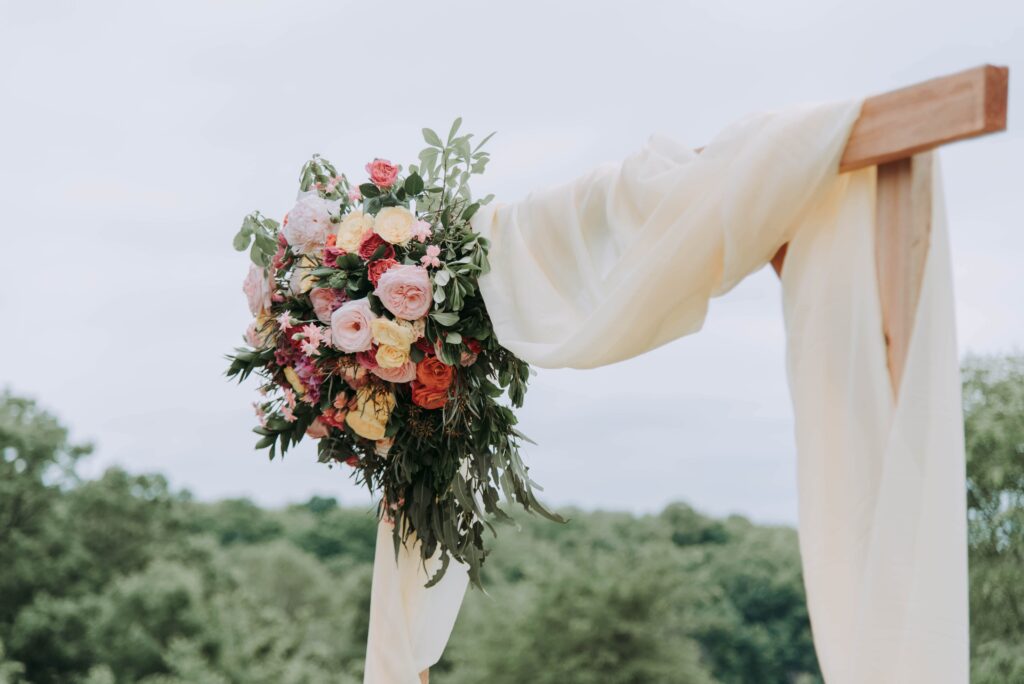Wedding Flowers on a wooden arch with flowy ivory fabric draped on it